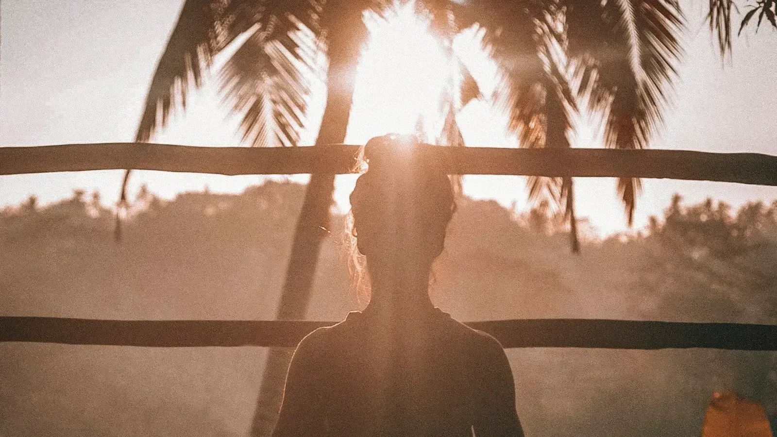 Personne assise en méditation devant des palmiers au coucher du soleil, image évoquant une respiration calme